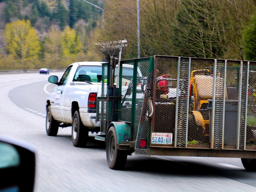 Pickup truck towing a trailer with landscaping equipment, driving on a highway.