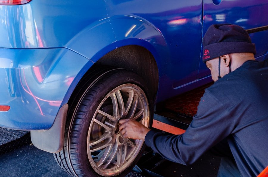 A mechanic works on the rear wheel of a blue car in a garage.