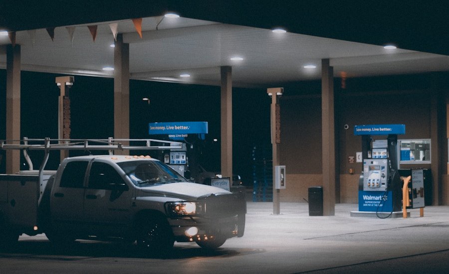 A white pickup truck is parked at a dimly lit gas station with two fuel pumps visible in the background.
